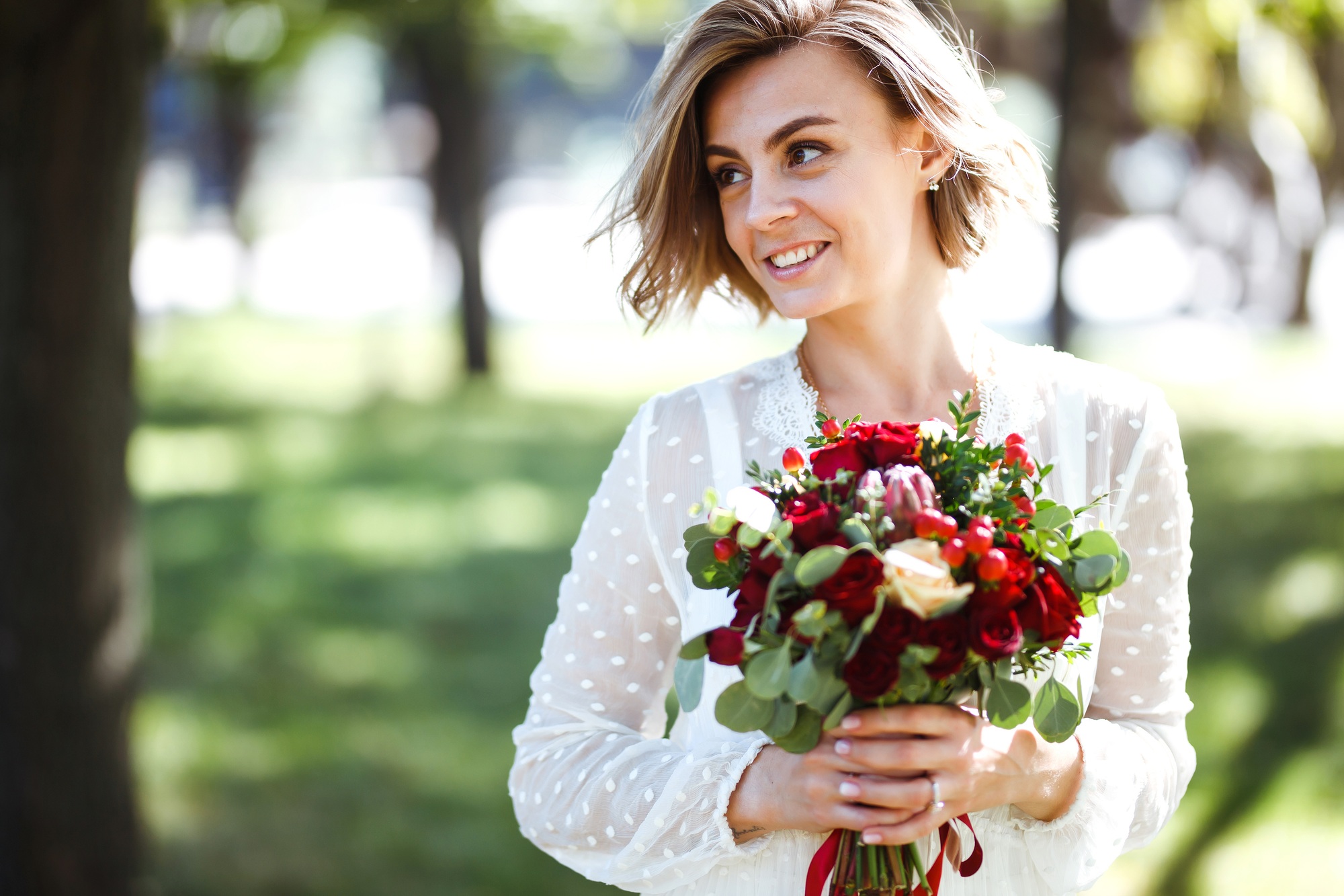Beautiful bride with wedding bouquet in park. Elegant woman with professional make up and hair style