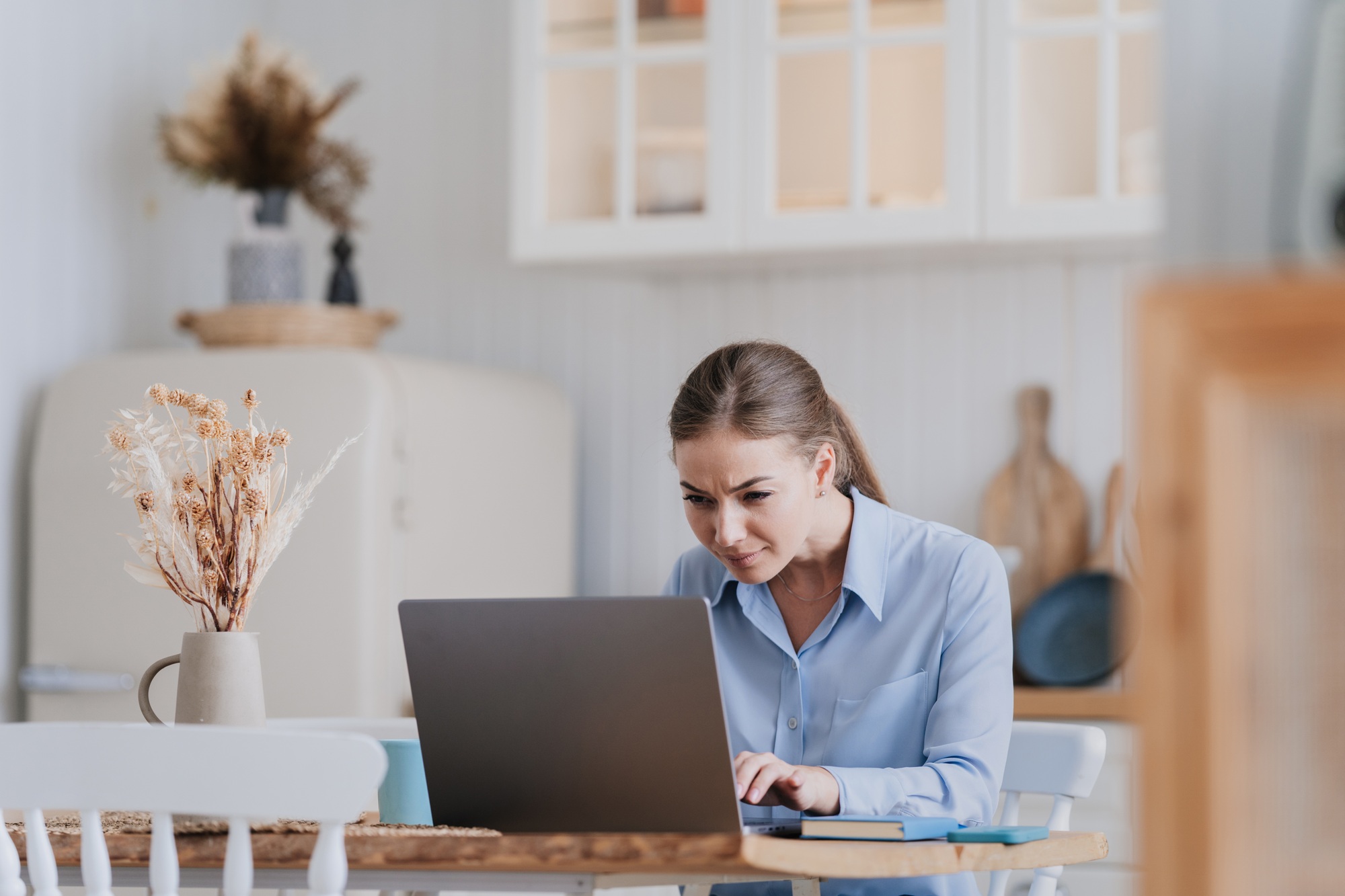 Focused blonde caucasian woman in shirt sits at desk with laptop looks at screen in disbelief